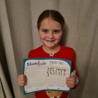 Little girl wearing a thumb guard and showing her reward chart