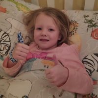 Little girl wearing a blue flower thumb glove in bed