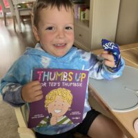 Little boy wearing a finger guard and showing his thumb sucking book
